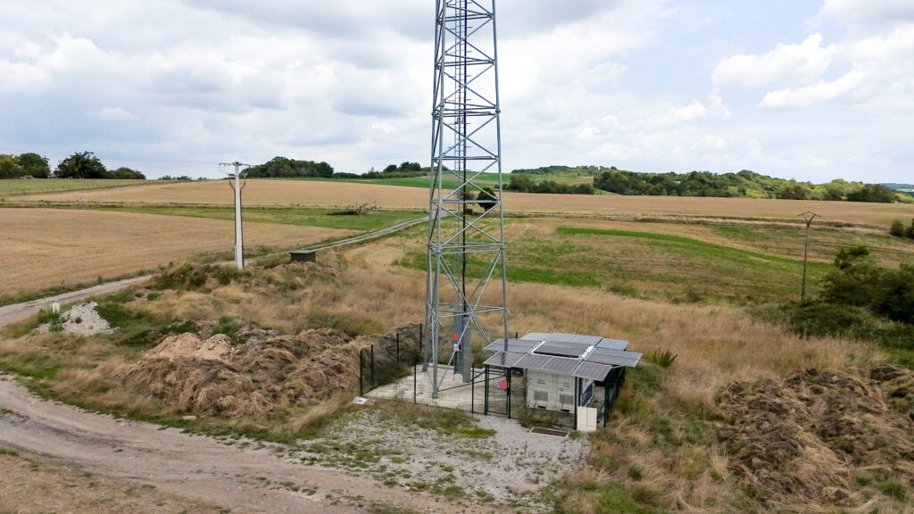 Vue aérienne d'un container hybride Revolt Location avec panneaux solaires déployés, alimentant une antenne relais isolée en plein champ.