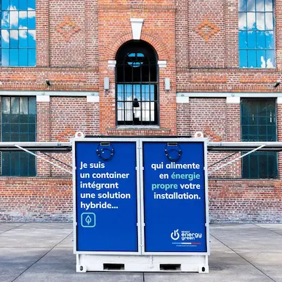 Un container d'énergie hybride Revolt Energy Green "Fabriqué en France" devant un bâtiment industriel historique en briques.