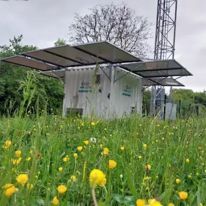Container solaire hybride Revolt Energy Green installé en milieu naturel à proximité d'un pylône de télécommunication.