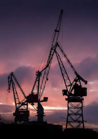 Silhouettes de grues portuaires industrielles au coucher du soleil pour illustrer les besoins en énergie décarbonée Revolt Energy Green.